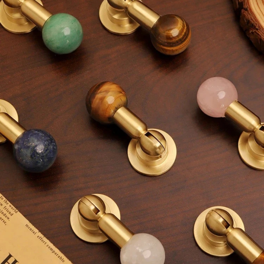 Modern brass cabinet knobs with brown gemstone sphere handles installed on grey drawers.
