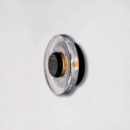 A close-up of the circular wall light showing the stone-textured surface and dark central core against a neutral background.