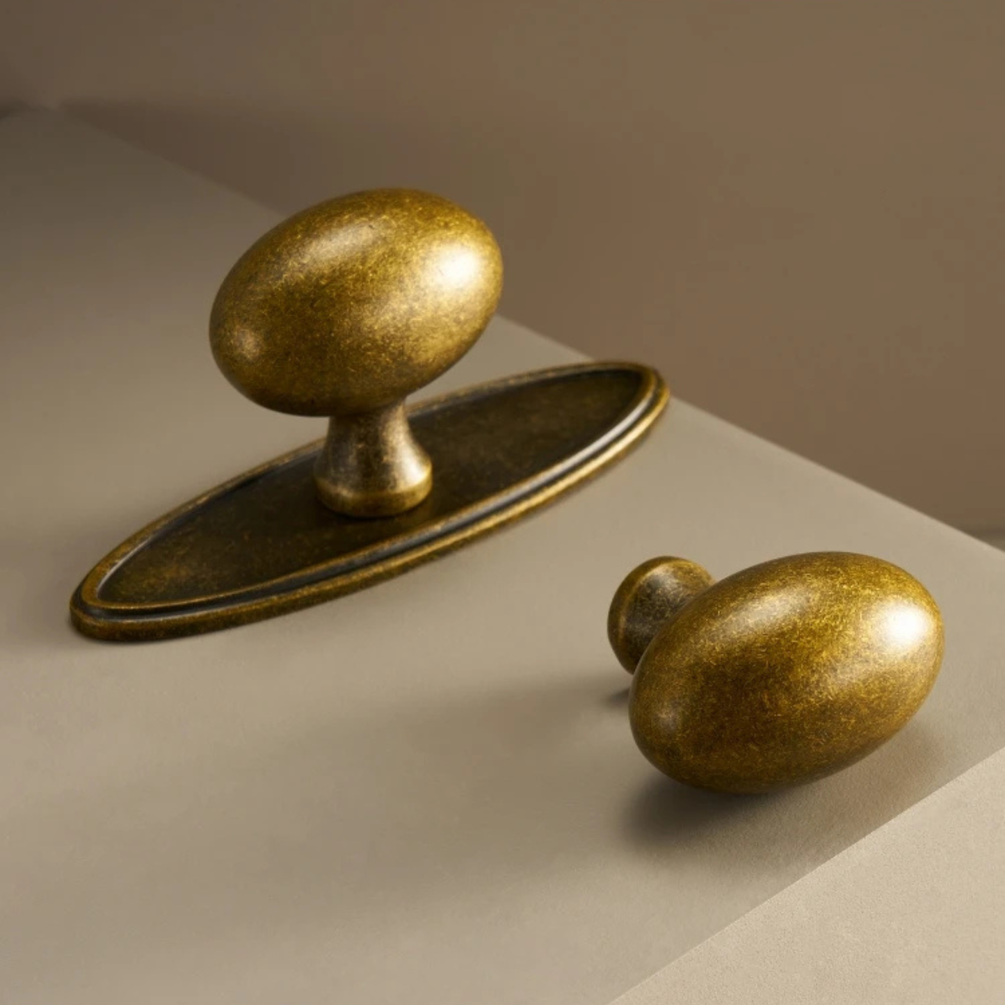 A pair of brass knobs with circular backplates displayed on a beige background.