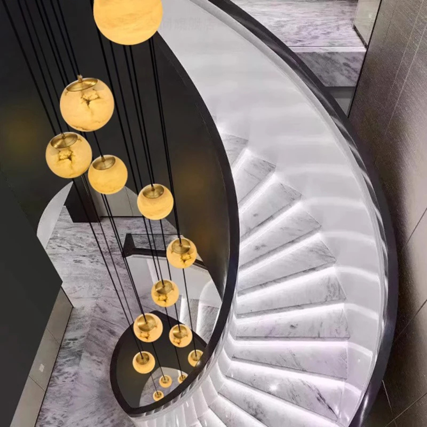 A vertical pendant light cluster with spherical lamps illuminating a stairwell with curved walls.