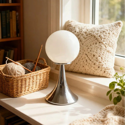 A white glass globe table lamp on a chrome base set on a woven mat beside rattan baskets and soft natural lighting.