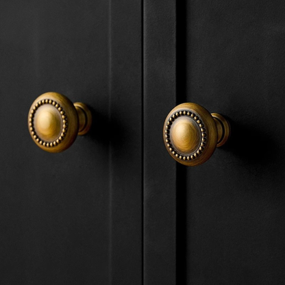 Two brass knobs attached to matte black cabinet doors, showing a classy contrast.