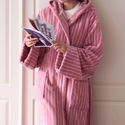 Person wearing a pink robe reading a magazine against a white wall.