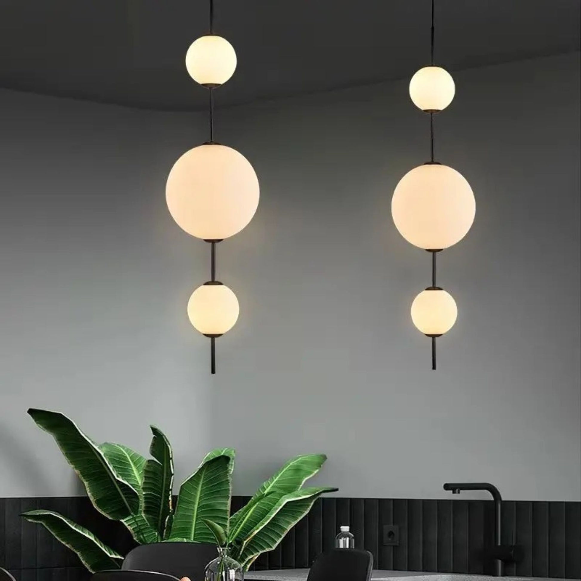 Three round globe lights hanging vertically, providing a soft glow in a modern living room with plants.