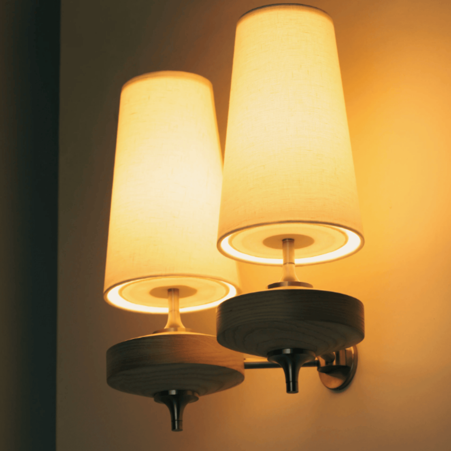 Wall-mounted lamp with two illuminated lampshades on a dark background