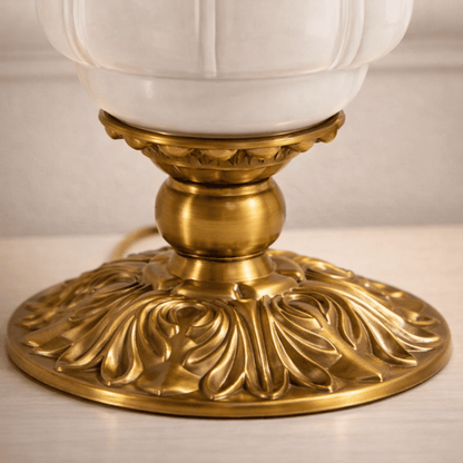 Decorative lamp with gold base and white glass shade on a neutral background