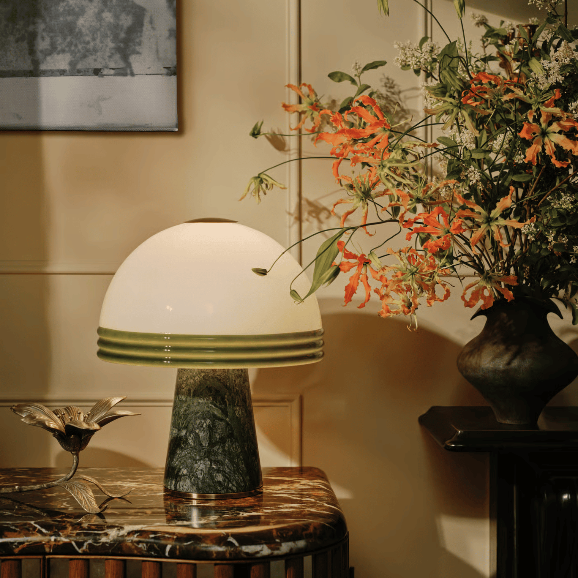 Table lamp with a green base and white shade on a marble table, next to a vase of flowers.