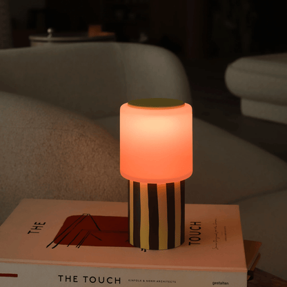 Small lamp with striped design on top of a book titled 'The Touch' in a cozy indoor setting.