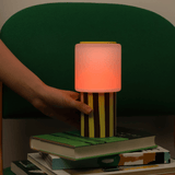 Hand holding a colorful striped lamp over a stack of books with a dark background