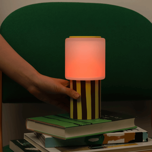 Hand holding a colorful striped lamp over a stack of books with a dark background