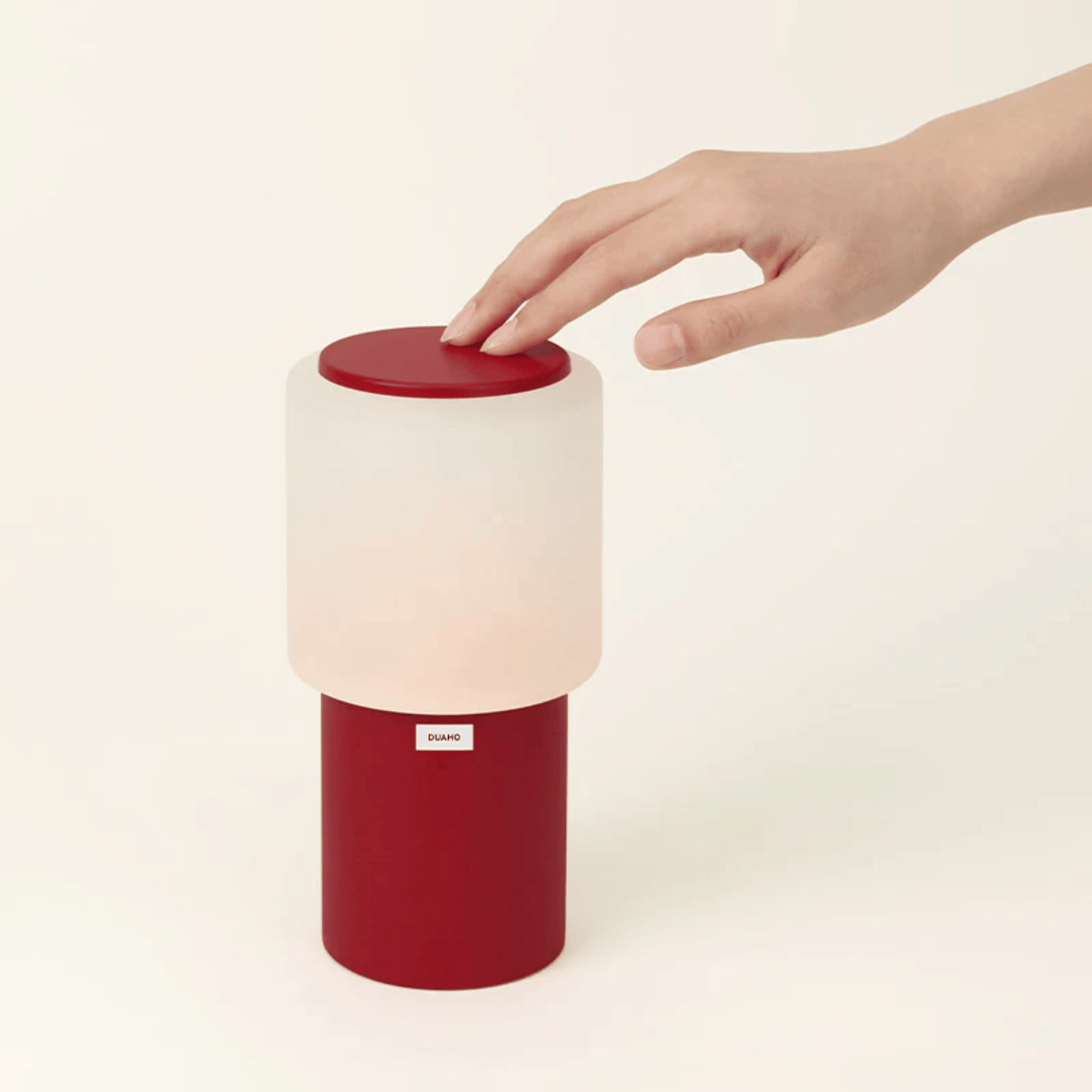 Red and white lamp with a hand pressing a button on a beige background