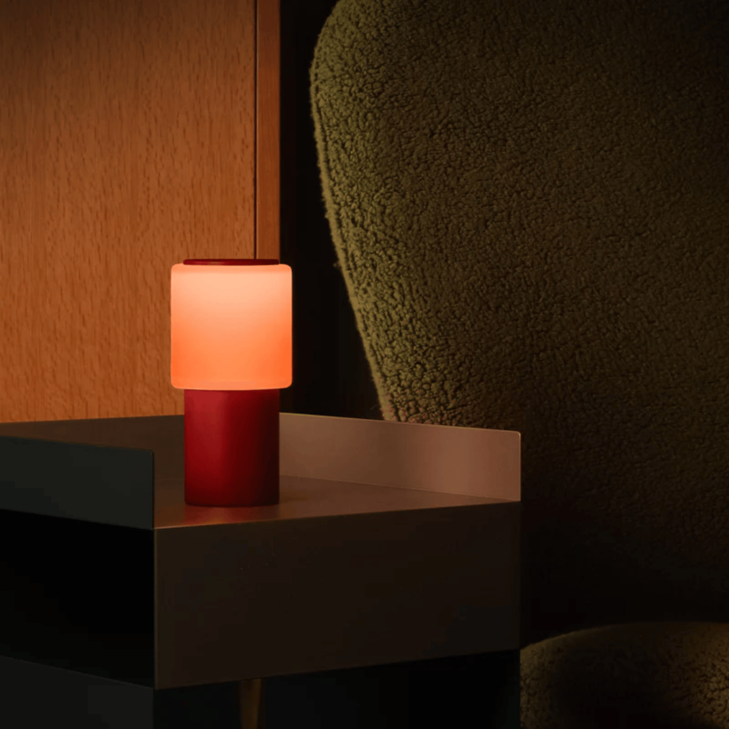 Small lamp with a red base and pink shade on a dark surface against a dark background