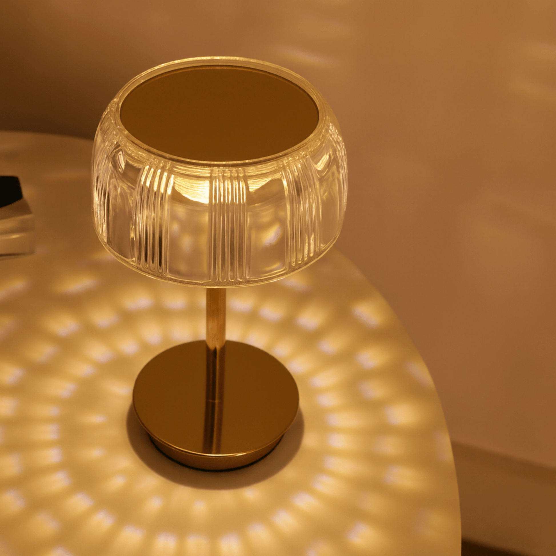 Gold table lamp with clear glass shade casting a warm glow on a surface.