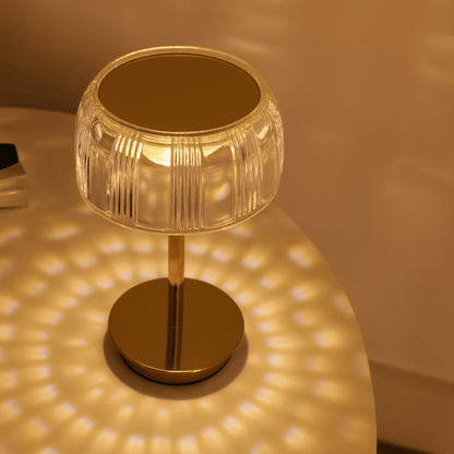 Gold table lamp with clear glass shade casting a warm glow on a surface.
