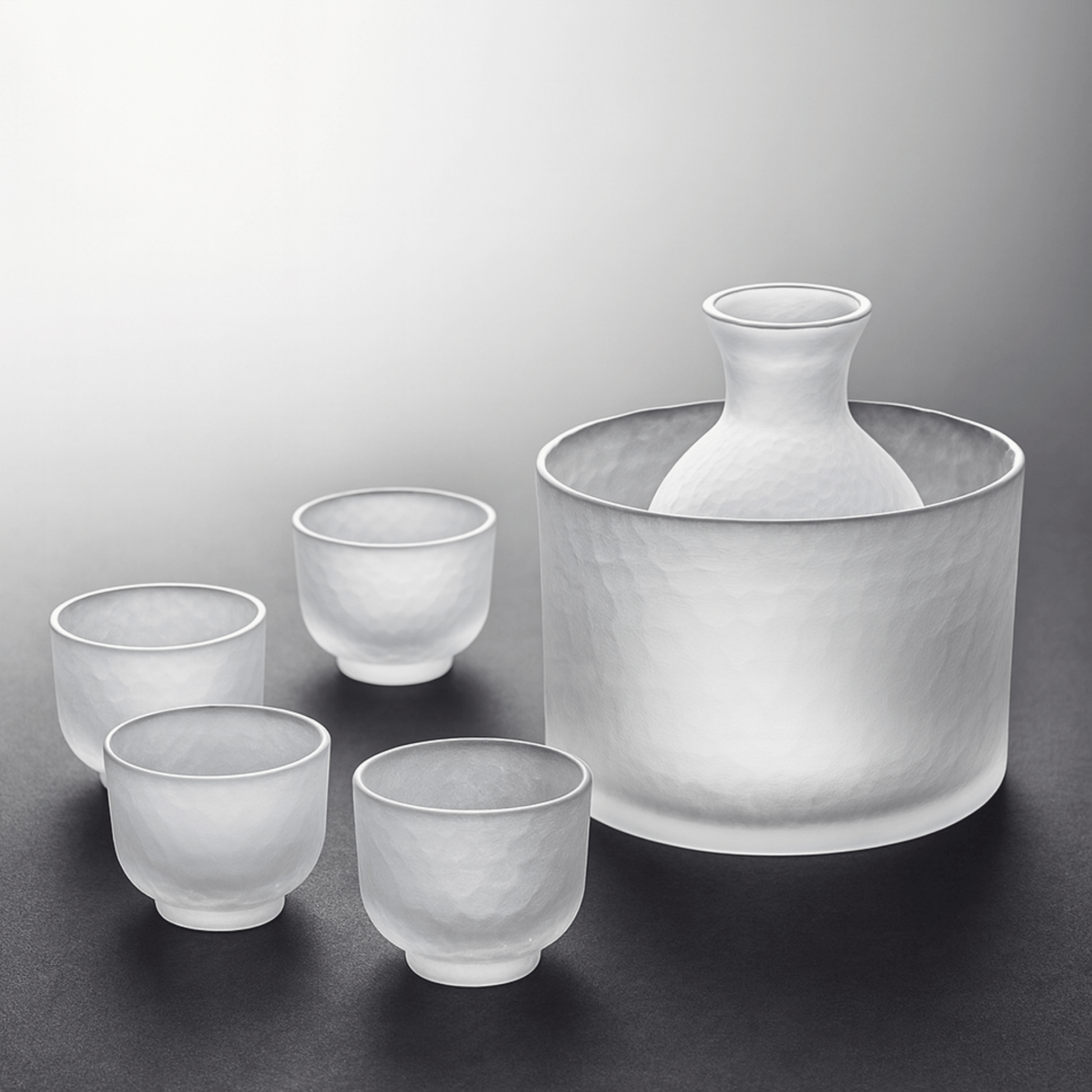Set of frosted glass sake cups and a large container on a gray background