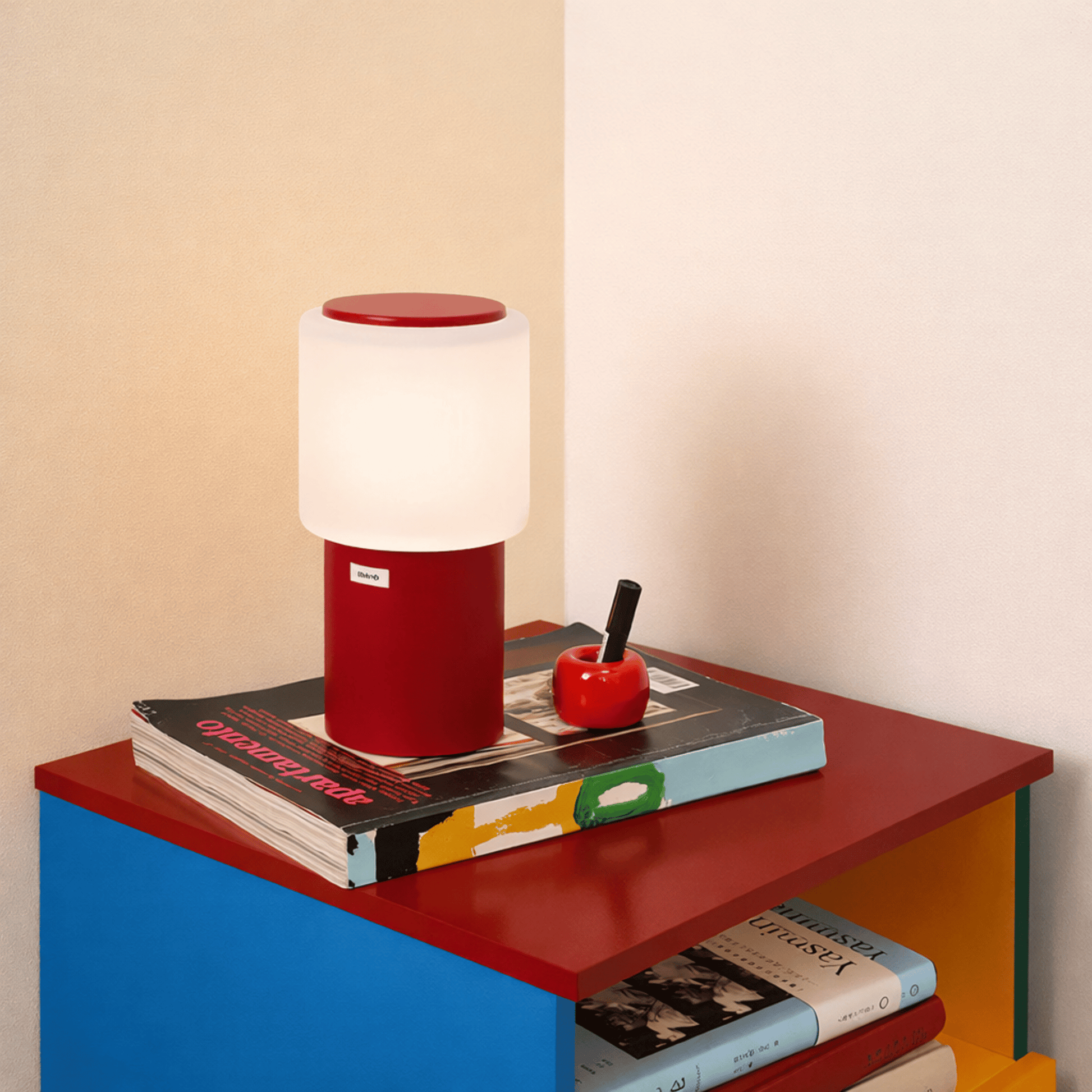 Red and white lamp on a colorful bookshelf with books and a small apple.