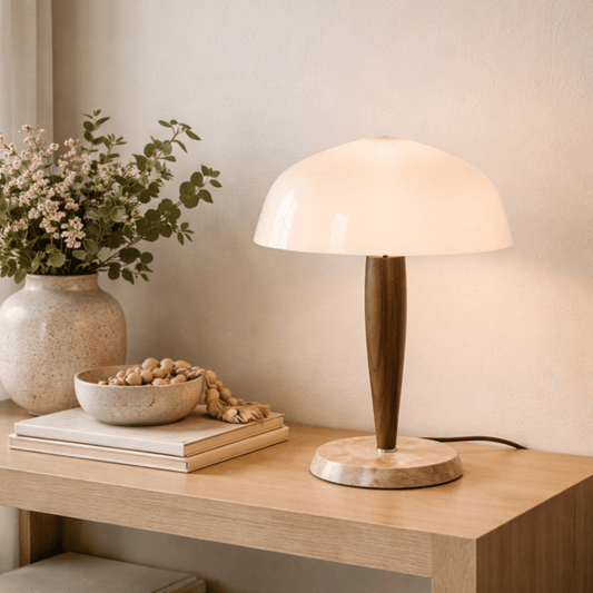 Table lamp on a wooden surface with a vase of flowers and a bowl of nuts in the background.