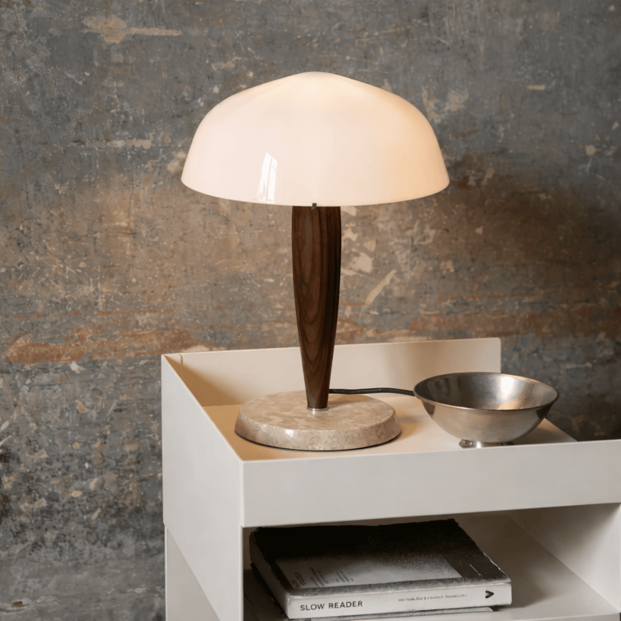 Table lamp with wooden base and white shade on a white surface against a textured wall.