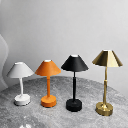 Four different colored table lamps on a gray surface with a gray background