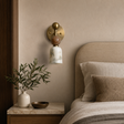 Decorative wall sconce above a bed with pillows and a plant on a nightstand.