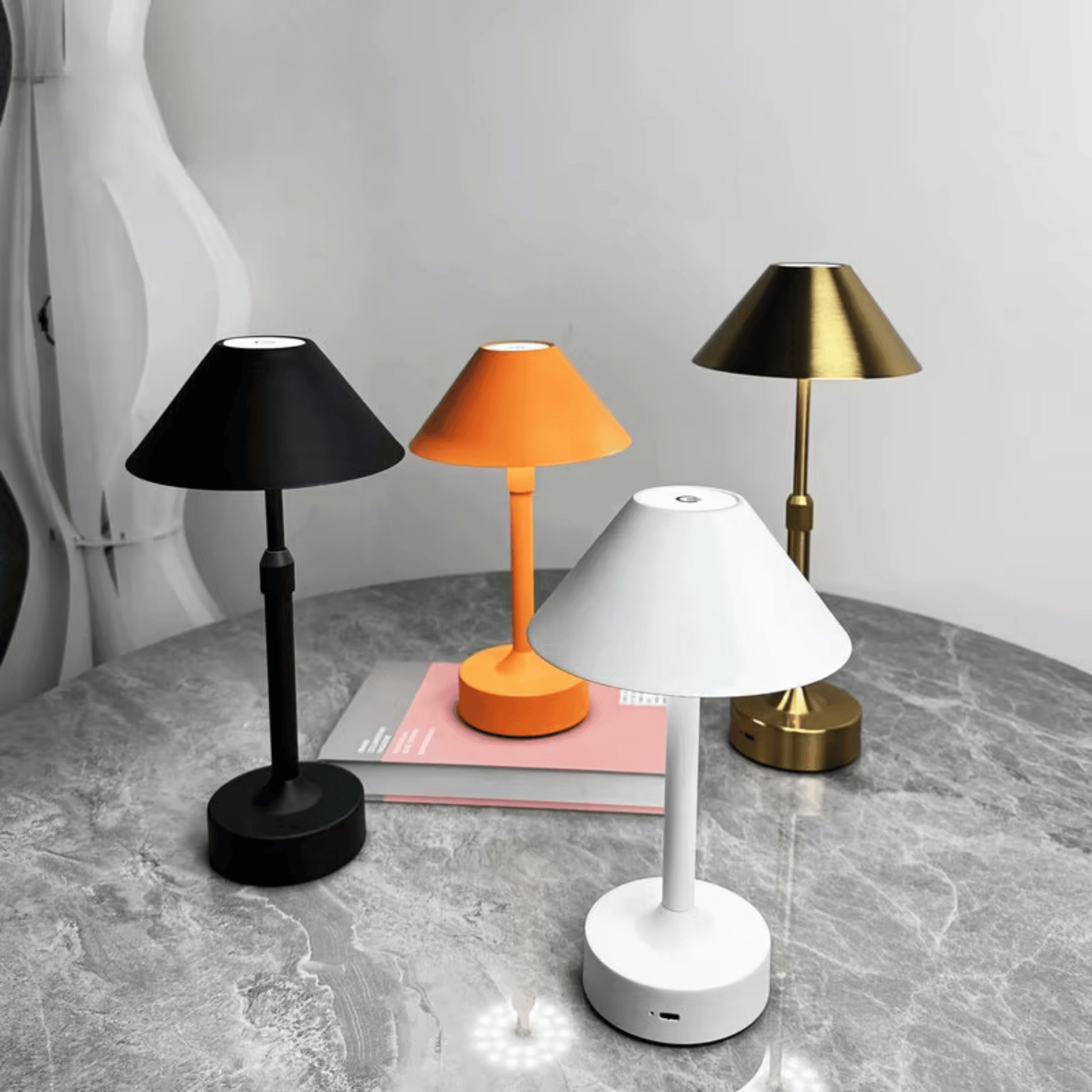 Four table lamps in black, orange, white, and gold on a gray surface with a white background.