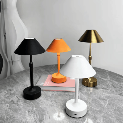 Four table lamps in black, orange, white, and gold on a gray surface with a white background.