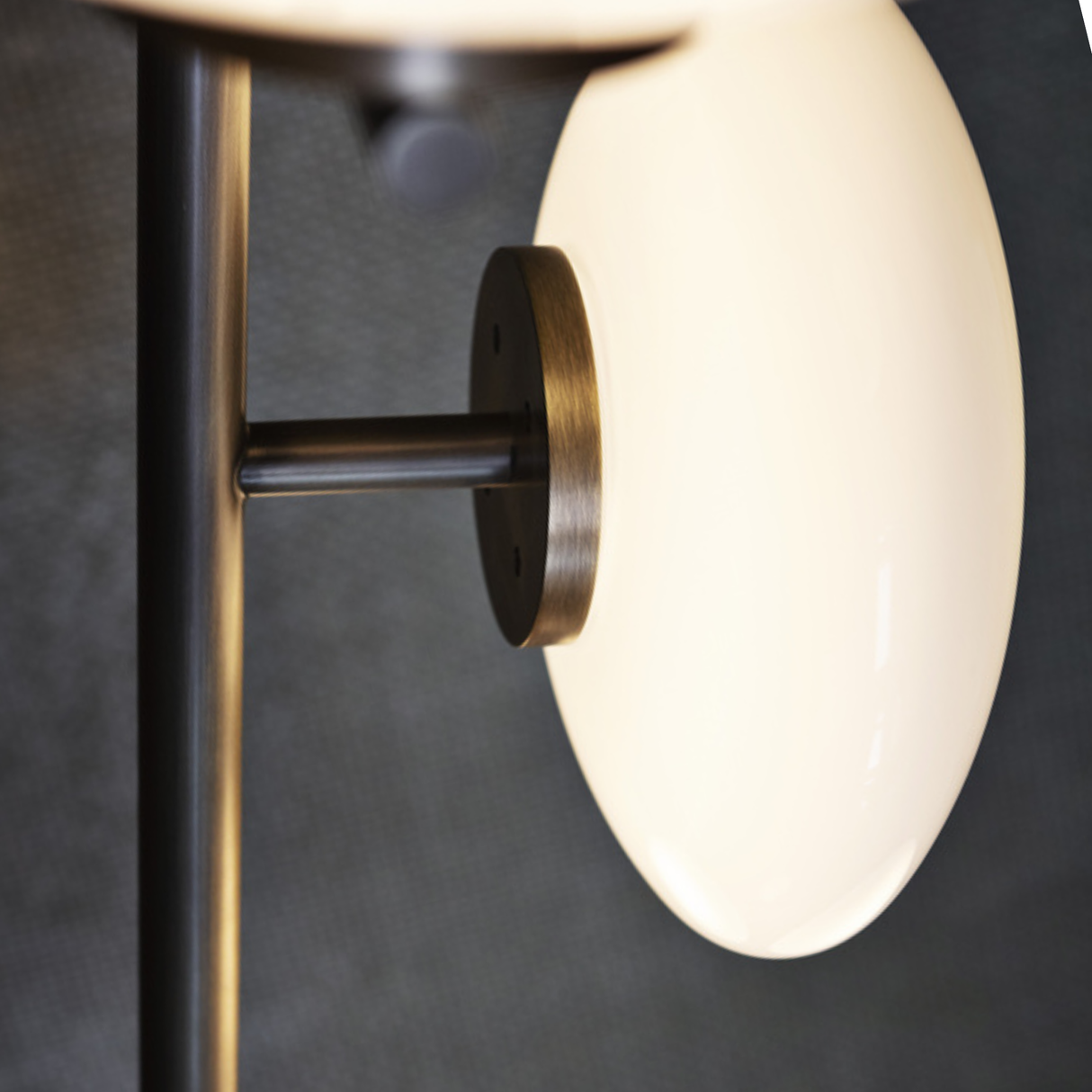 Wall-mounted light fixture with bronze finish and white glass shade on a dark background