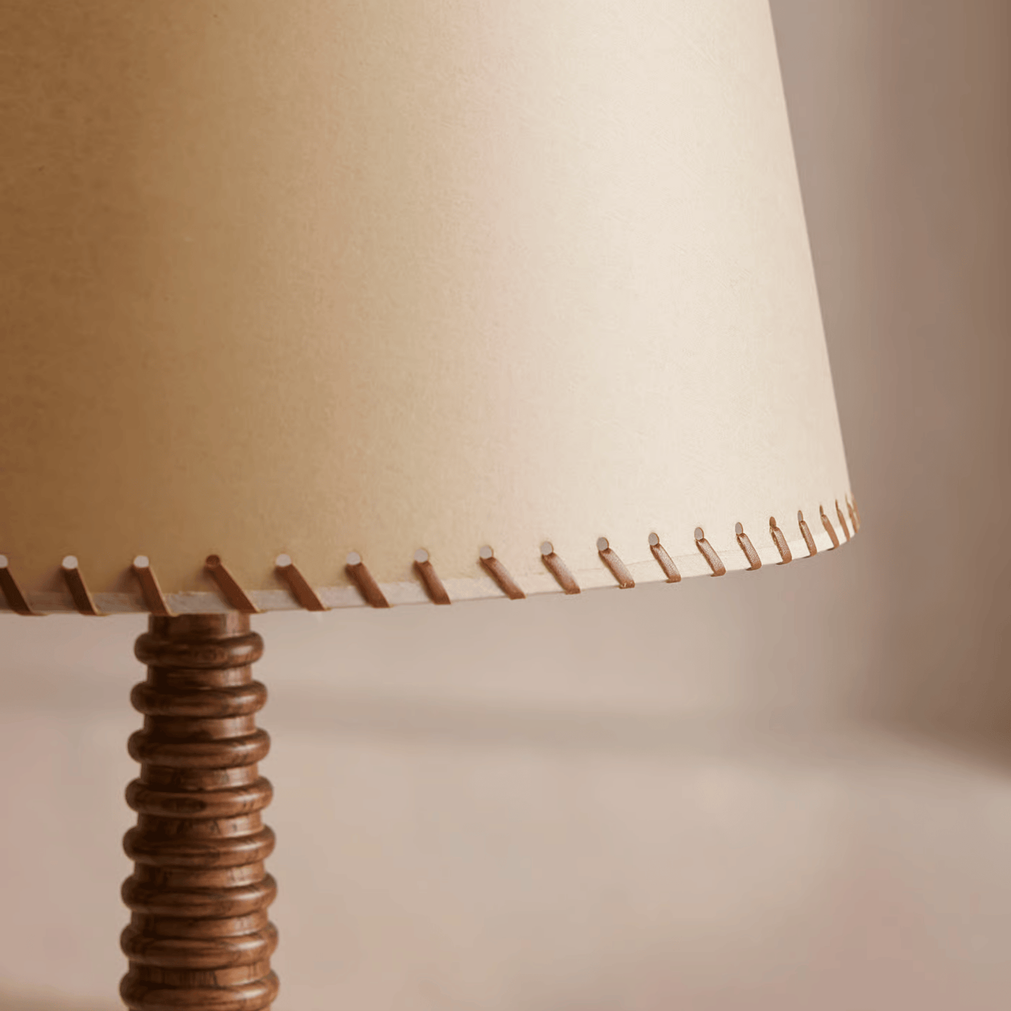 Close-up of a lamp with a beige shade and wooden base on a neutral background