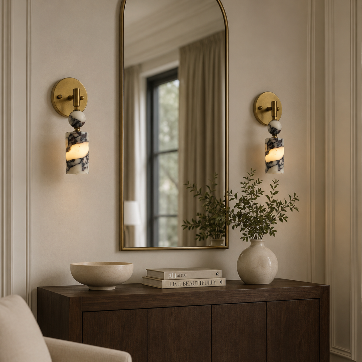 Decorative wall sconces, mirror, and books on a wooden console table in a room.