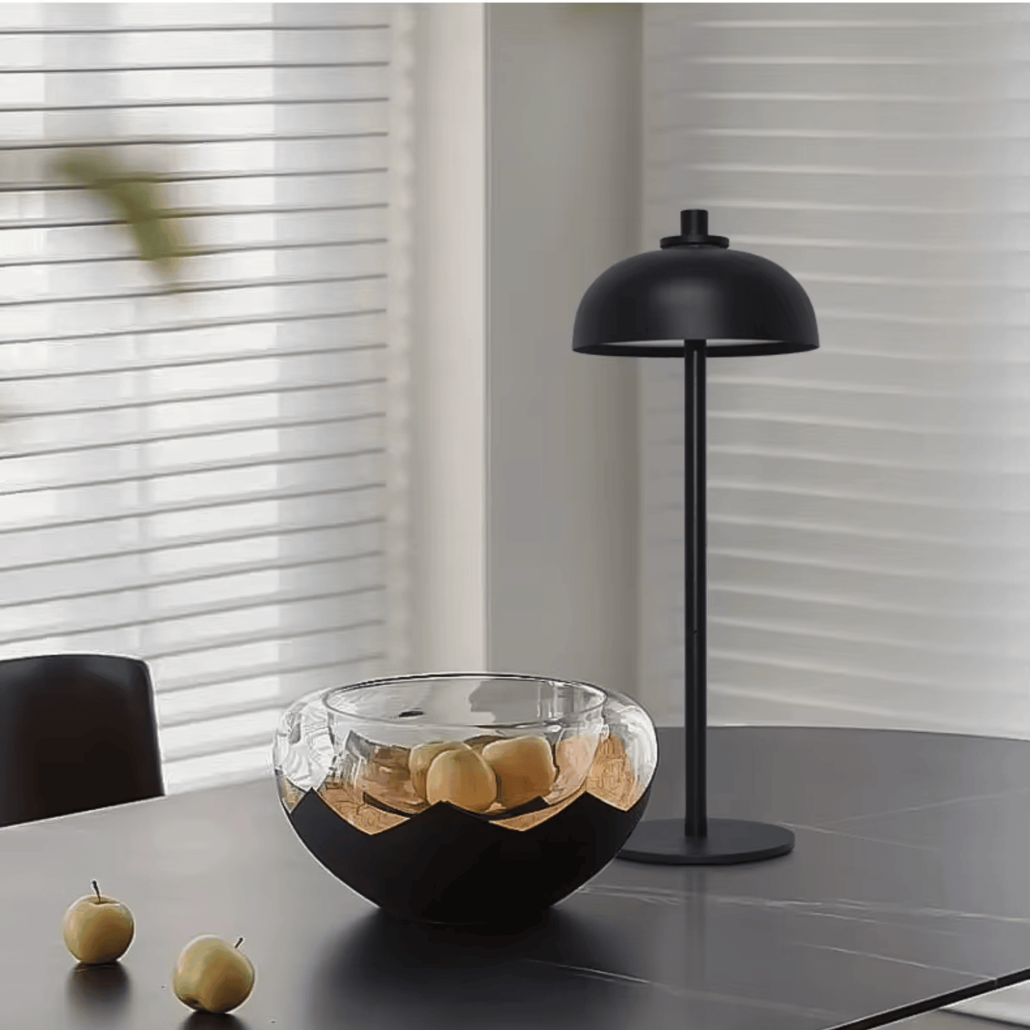 Modern black lamp and glass bowl on a table with apples in a minimalistic setting.