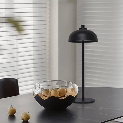 Modern black lamp and glass bowl on a table with apples in a minimalistic setting.