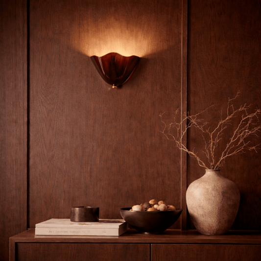 Decorative wall sconce, vase, and books on a wooden surface with a warm brown background.