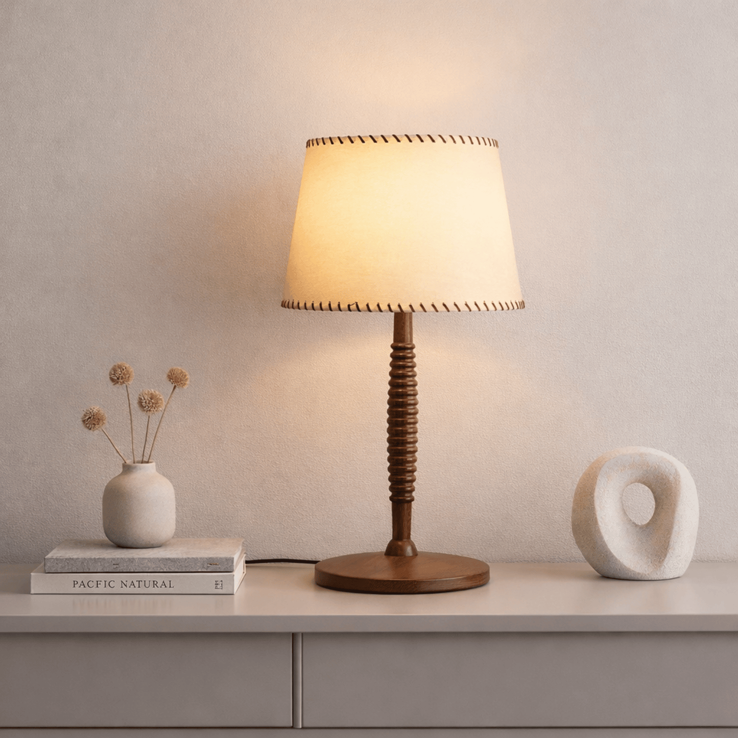 Table lamp with wooden base and beige shade on a surface with decorative items.