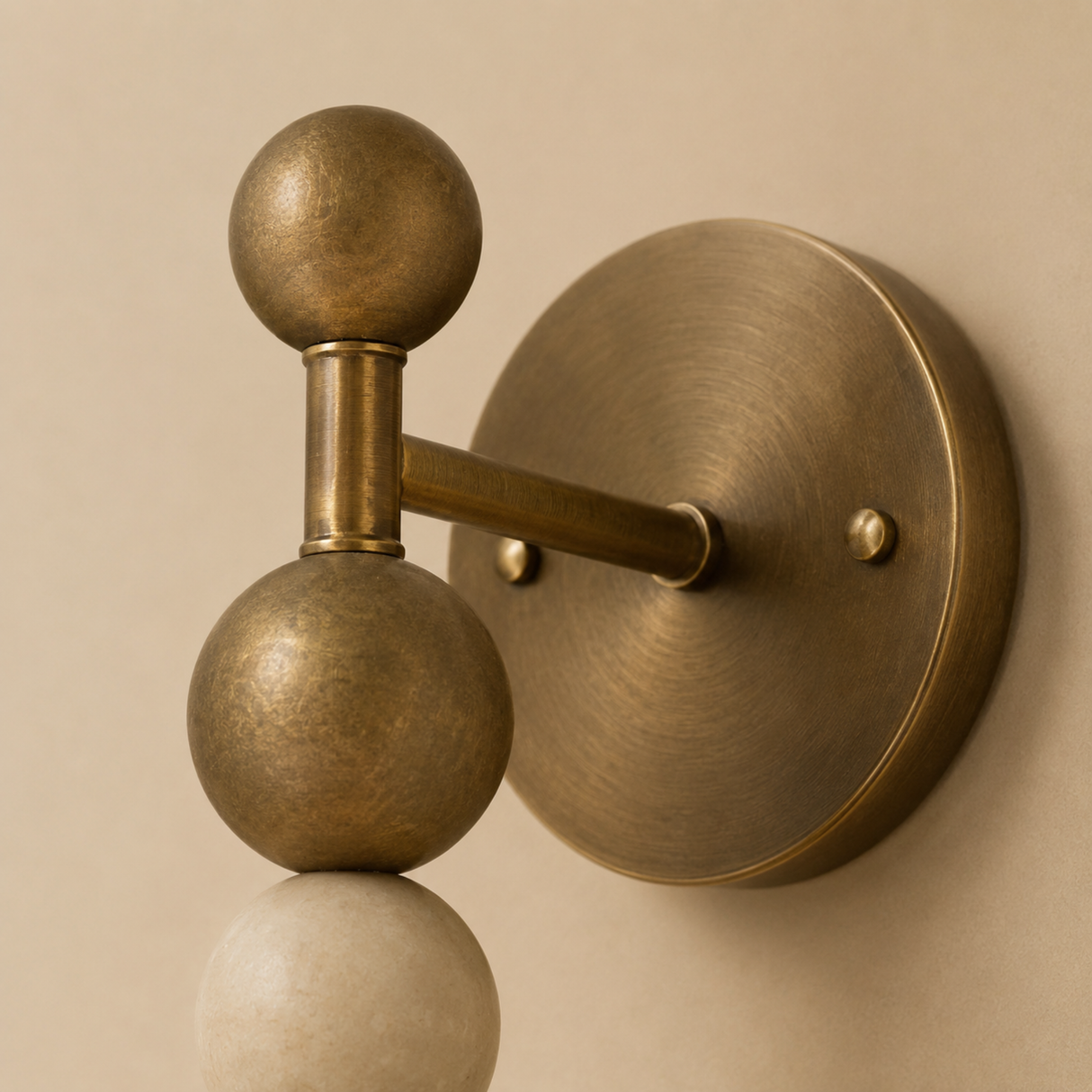 A close-up of a wall-mounted decorative light fixture with two spherical bulbs on a curved arm, finished in an antique brass or bronze tone against a warm beige wall.