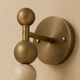 A close-up of a wall-mounted decorative light fixture with two spherical bulbs on a curved arm, finished in an antique brass or bronze tone against a warm beige wall.