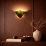 Decorative wall sconce with a green glass shade on a brown paneled wall.