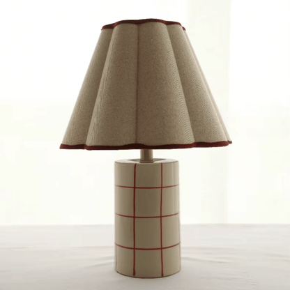 Table lamp with a textured beige shade and a cylindrical base with red grid pattern on a white background