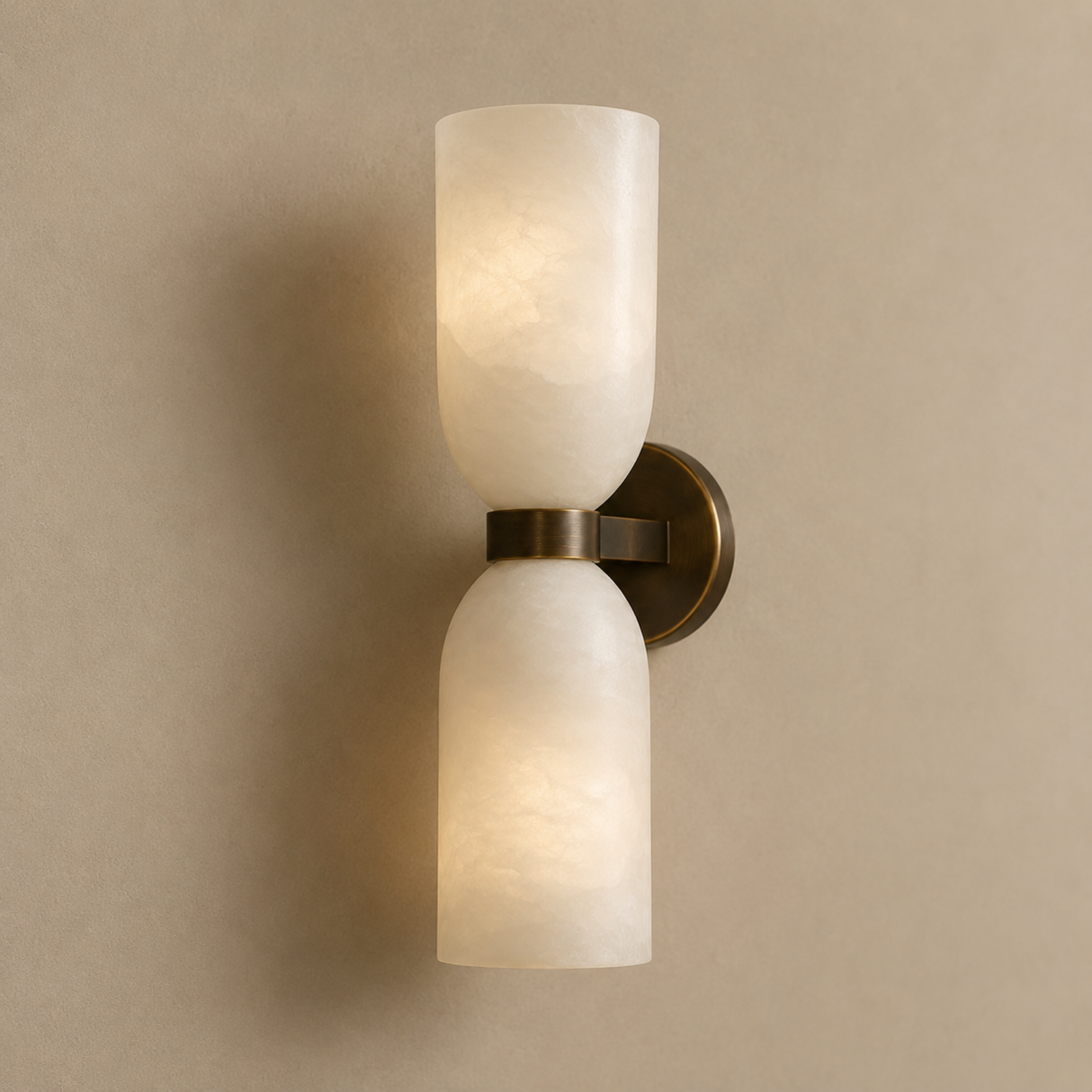 A modern two-light wall sconce with frosted white glass cylindrical shades and a brushed bronze metal mount, shown lit against a warm beige wall.