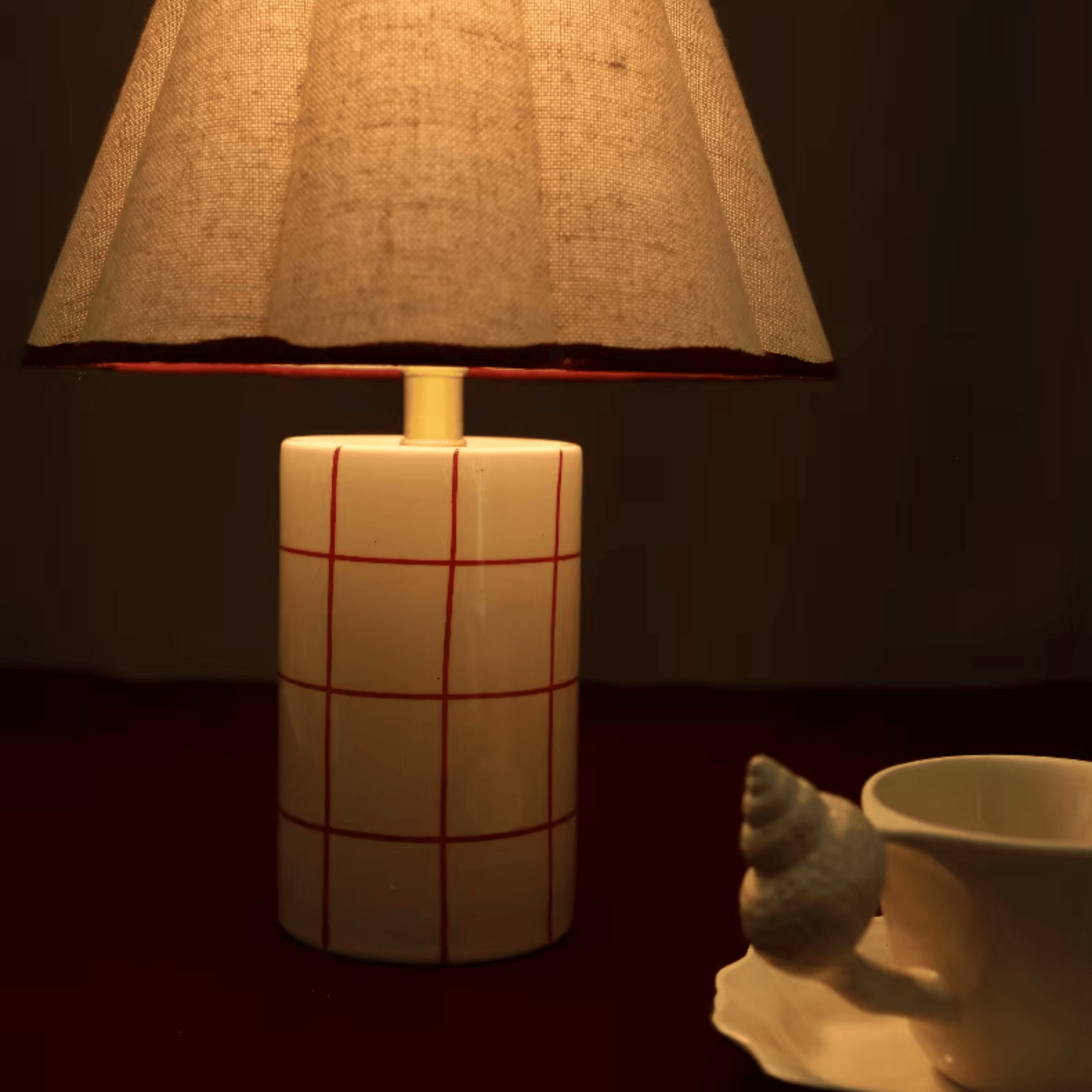Lamp with a textured shade and grid-patterned base next to a mug on a dark background