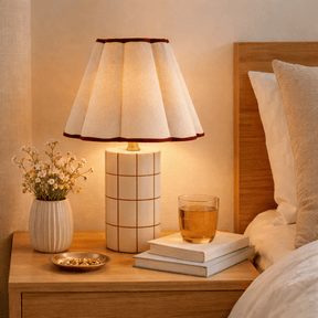 Lamp on a bedside table with books, a glass of tea, and a vase of flowers in a cozy bedroom setting.