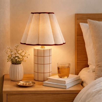 Lamp on a bedside table with books, a glass of tea, and a vase of flowers in a cozy bedroom setting.