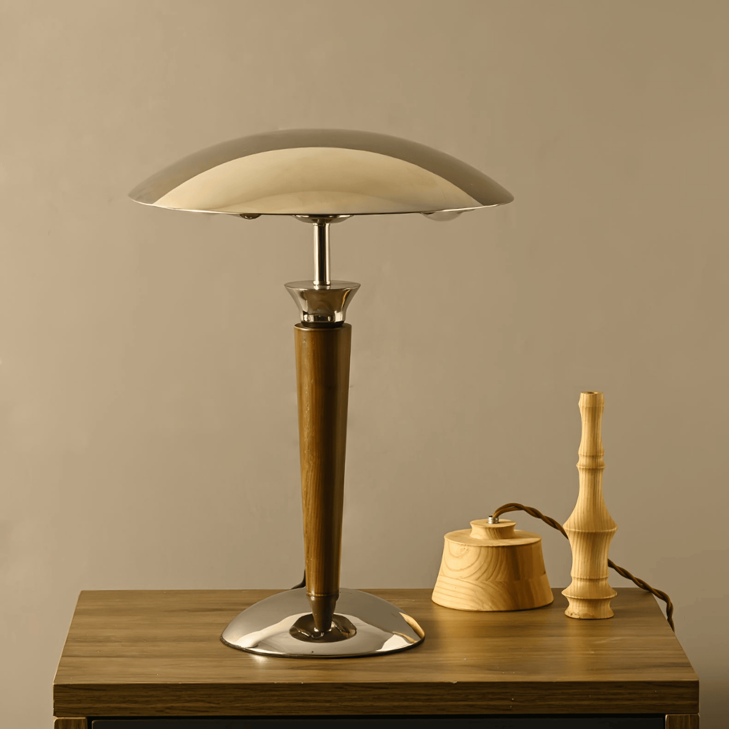 Table lamp with wooden base and beige shade on a wooden surface against a beige wall.