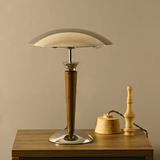 Table lamp with wooden base and beige shade on a wooden surface against a beige wall.