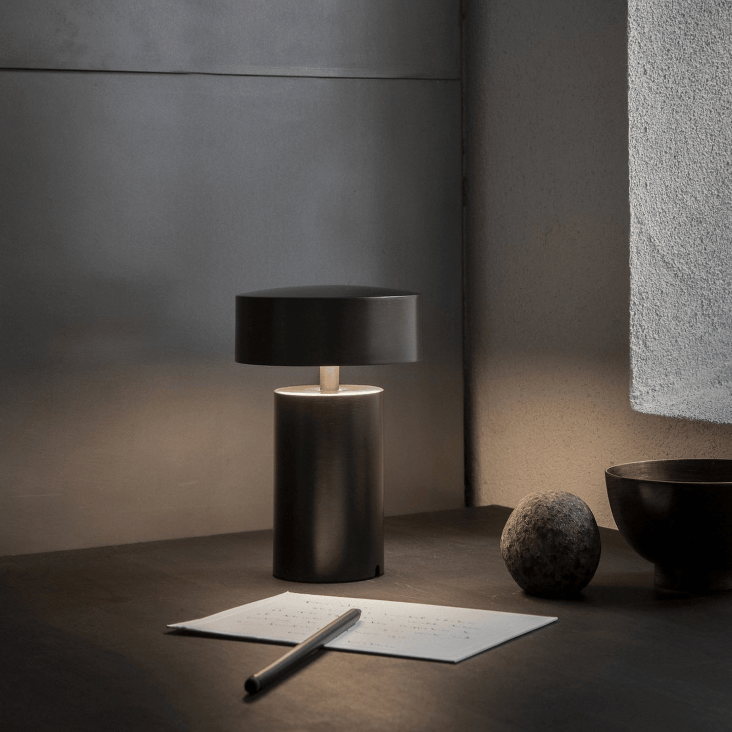 Dark table lamp on a surface with a pen and paper in a minimalistic setting.