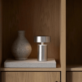 Silver lamp and textured vase on a wooden shelf