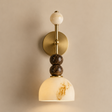 A wall-mounted sconce with a round brass backplate, a vertical brass stem, a cream marble sphere at the top, two stacked dark brown marbled beads, and a dome-shaped cream marble shade with warm gold veining, shown against a beige wall.