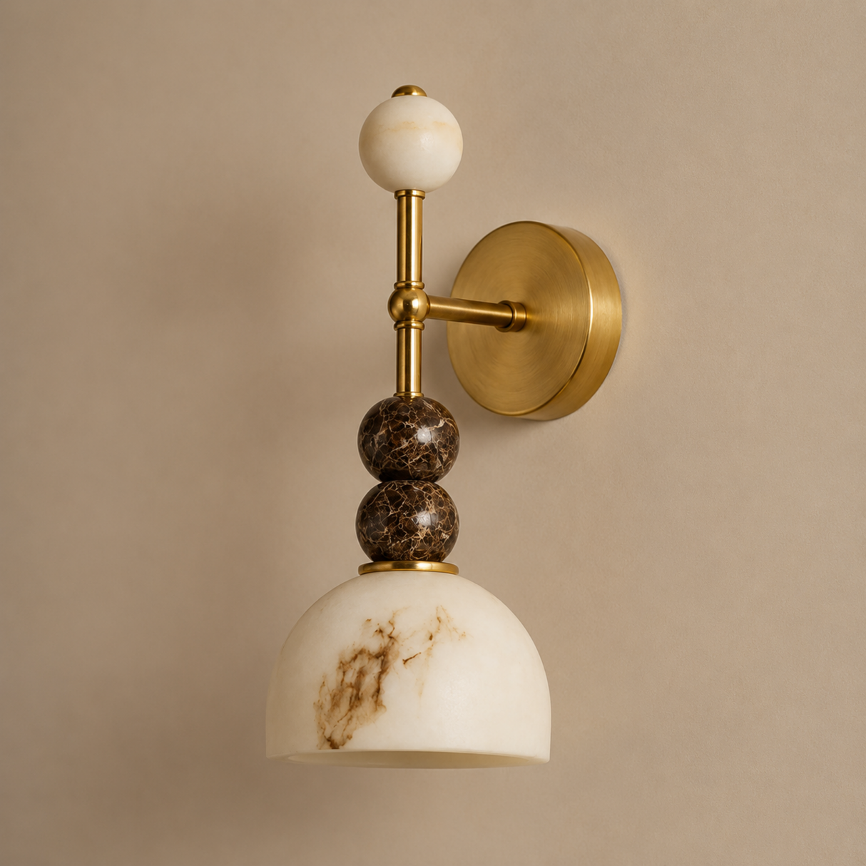 A wall-mounted sconce with a round gold brass backplate, a vertical gold stem, a white marble sphere finial, two stacked dark brown marble beads, and a white marble dome shade with brown veining, shown against a warm beige wall.