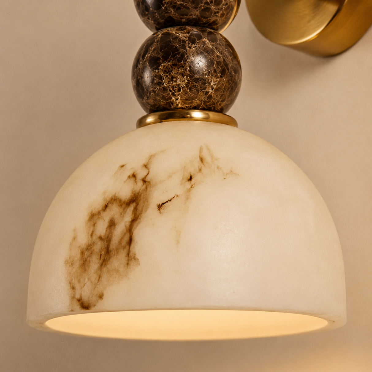 A close-up of a wall-mounted light fixture with a large dome-shaped off-white marble shade featuring dark brown veining, supported by stacked dark marble spheres with gold-toned metal accents.