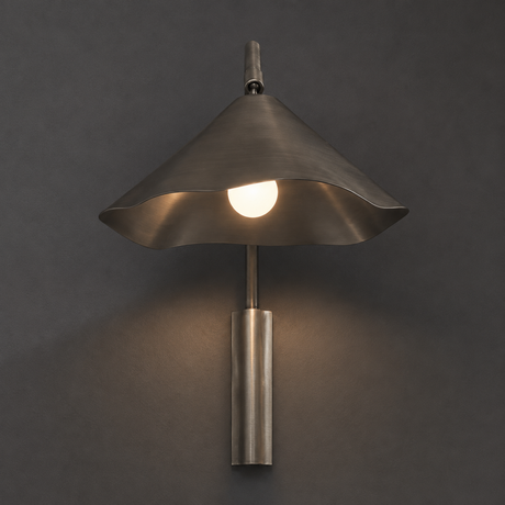 A modern wall-mounted sconce with a flared brushed metal shade and a cylindrical base, shown lit against a dark gray wall.