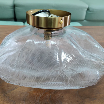 Clear glass lampshade with gold metal fixture on a wooden surface